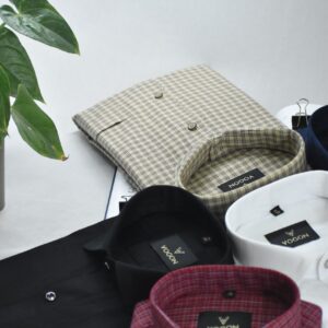 An assortment of folded shirts neatly arranged on a surface next to a green plant.